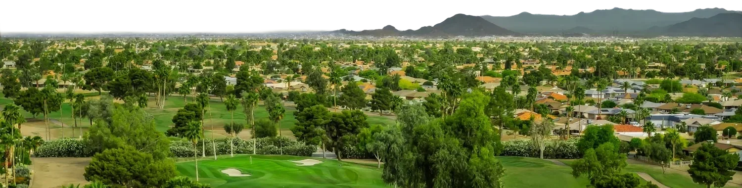 Panoramic aerial view of a golf course, surrounding homes and distant desert mountains.